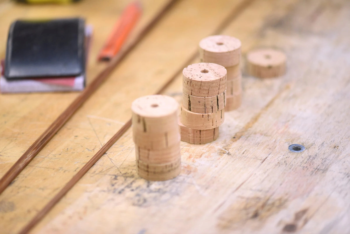 Stacked rings of Portuguese cork prepared for shaping into a bamboo fly rod grip, with sandpaper on a workbench.