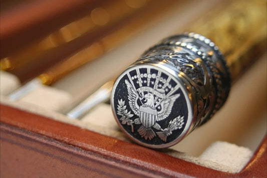 A hand-engraved nickel silver buttcap on a bamboo fly rod, featuring a deep-relief Presidential Seal with the bald eagle, shield, and 'E Pluribus Unum' banner, resting in rod case.