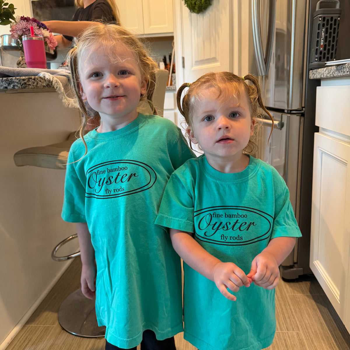 Two children wearing Oyster Fly Rods youth t-shirts in teal green. 