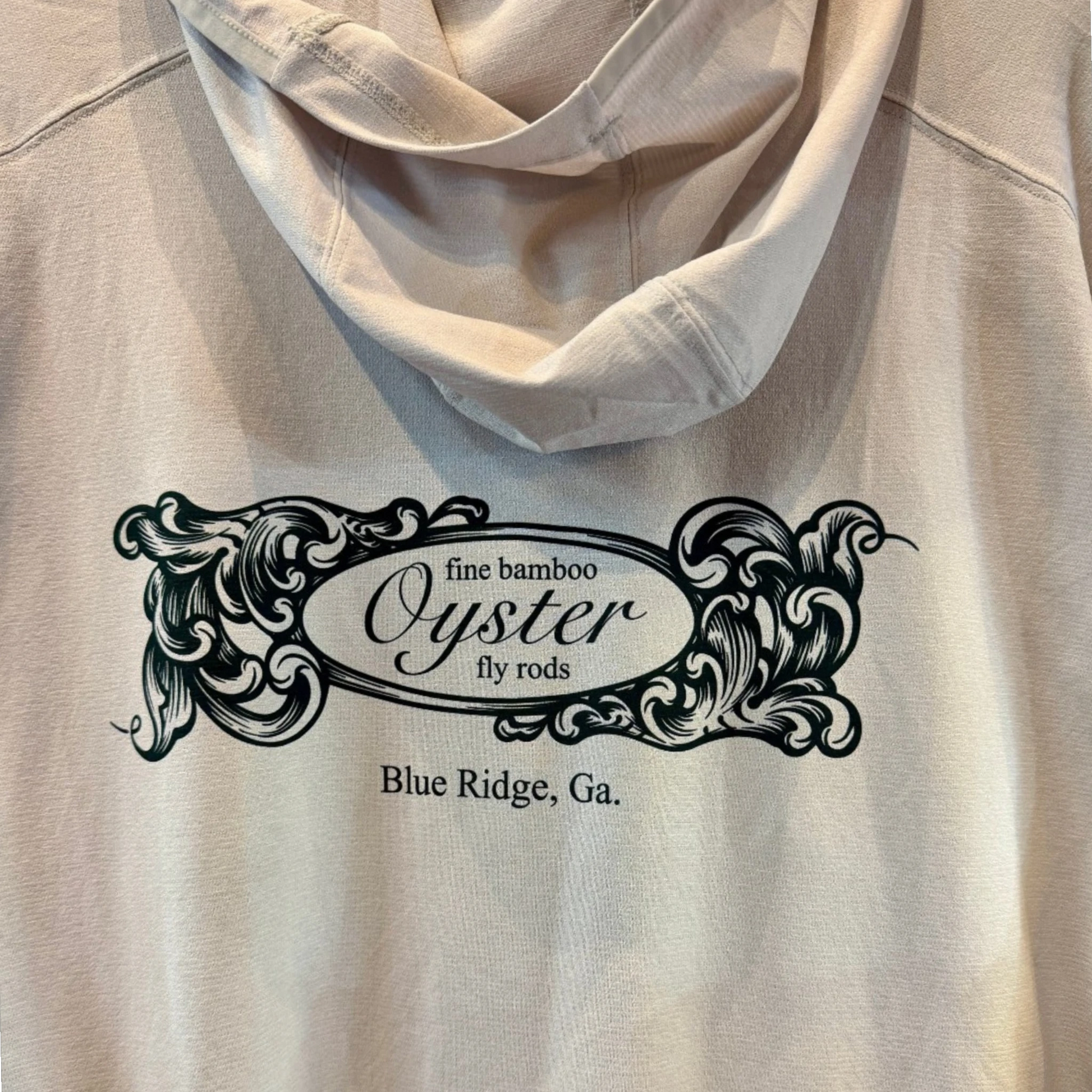 A close-up of Simms Solarflex hoody in overcast with a black graphic print on the back that reads 'fine bamboo Oyster fly rods Blue Ridge, Ga.' with ornate scrollwork.
