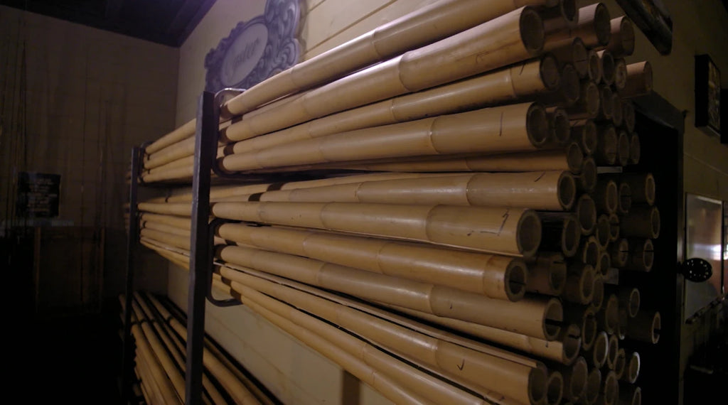 Tonkin bamboo culms stacked on a rack in a fly rod workshop, with an 'Oyster' sign in the background.
